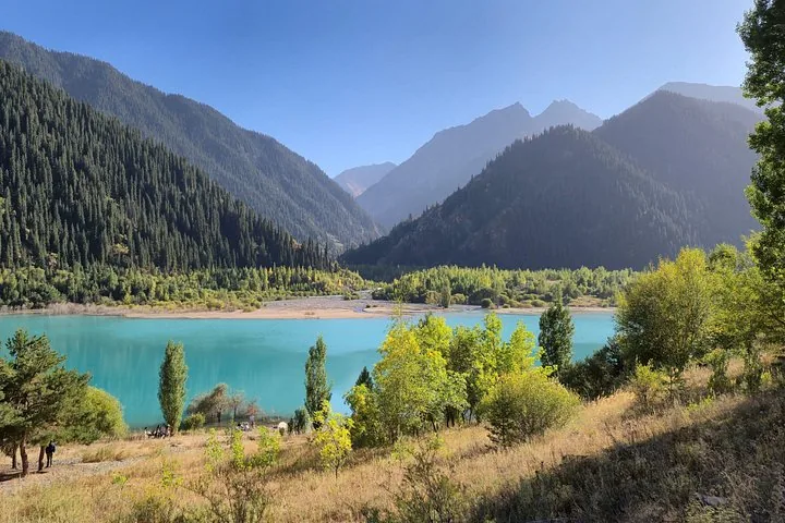 Ein türkisfarbener See, umgeben von Bäumen und Bergen im Ile-Alatau-Nationalpark.