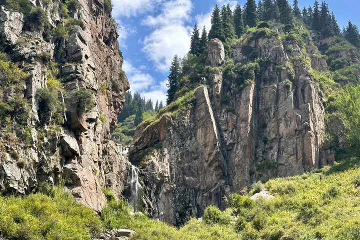 Ein Wasserfall stürzt eine steile felsige Klippe hinab, umgeben von grüner Vegetation und Bäumen.