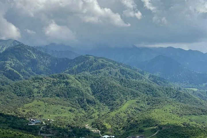 Una amplia vista de montañas verdes onduladas bajo un cielo nublado en el Parque Nacional Ile-Alatau.